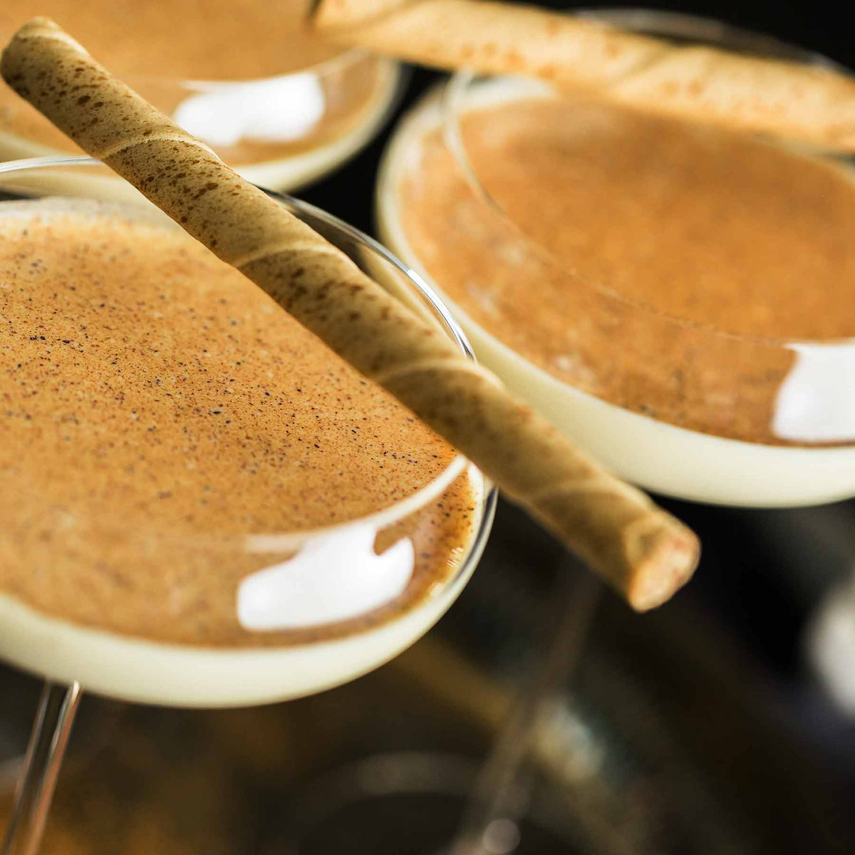 Two glasses of egg nog cocktail with a cinnamon stick on a blurred background; https://cdn.shopify.com/videos/c/o/v/6c853f172a9741559c892ae097293f2e.mp4